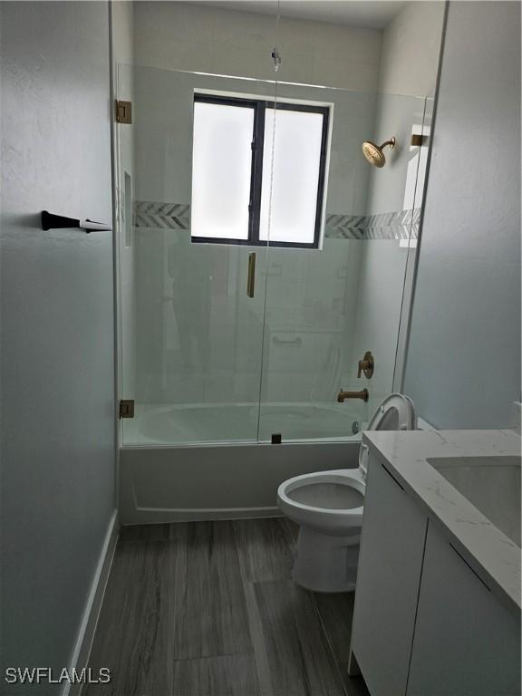 bathroom featuring baseboards, toilet, vanity, wood finished floors, and washtub / shower combination