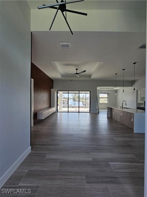 unfurnished living room with visible vents, dark wood-type flooring, a sink, a tray ceiling, and ceiling fan