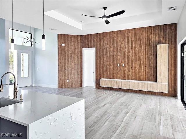 living room with visible vents, a tray ceiling, ceiling fan, light wood-style floors, and wood walls