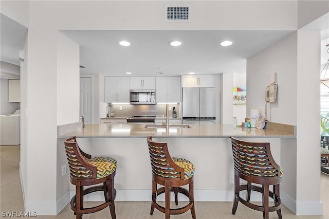 kitchen with stainless steel appliances, sink, white cabinetry, kitchen peninsula, and a breakfast bar