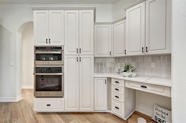 kitchen with backsplash, white cabinets, light stone countertops, light wood-type flooring, and stainless steel double oven