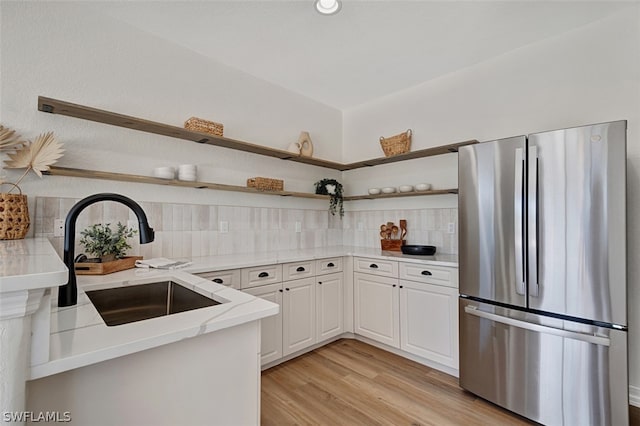 kitchen with stainless steel refrigerator, sink, light hardwood / wood-style flooring, backsplash, and white cabinets