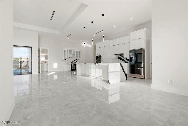 interior space featuring marble finish floor, a high ceiling, white cabinets, refrigerator with ice dispenser, and a large island with sink