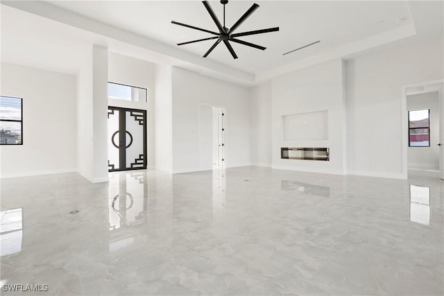 unfurnished living room with a tray ceiling, a wealth of natural light, and a glass covered fireplace