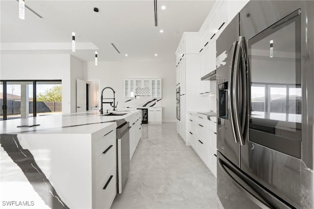 kitchen with a large island, marble finish floor, stainless steel appliances, white cabinetry, and a sink