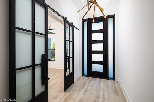 foyer entrance featuring a barn door, light hardwood / wood-style floors, and an inviting chandelier