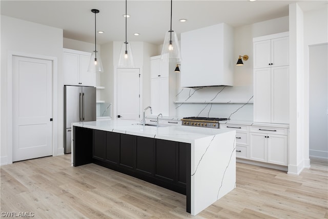 kitchen featuring white cabinets, an island with sink, light hardwood / wood-style floors, and decorative light fixtures