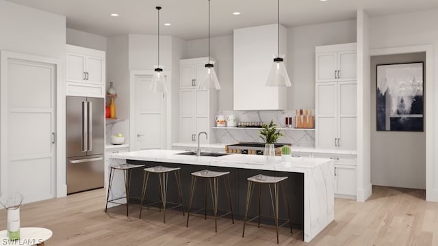 kitchen featuring a kitchen bar, a center island with sink, stainless steel refrigerator, and light wood-type flooring