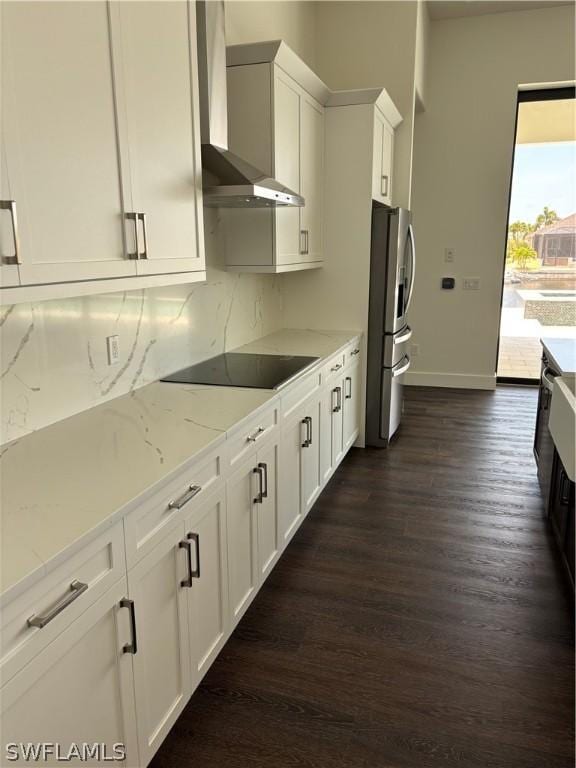 kitchen featuring white cabinets, wall chimney range hood, stainless steel refrigerator with ice dispenser, light stone countertops, and black electric cooktop