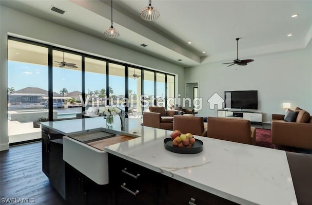 kitchen featuring dark hardwood / wood-style flooring, light stone counters, ceiling fan, a kitchen island with sink, and hanging light fixtures