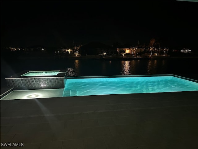 pool at night with an in ground hot tub and a water view