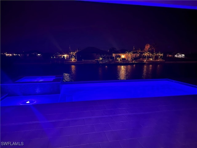 pool at twilight featuring a water view and an in ground hot tub