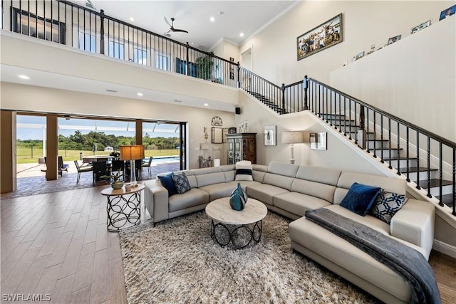 living room with hardwood / wood-style floors, crown molding, ceiling fan, and a towering ceiling