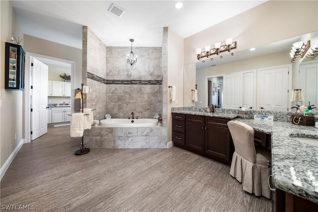 bathroom featuring a chandelier, tiled tub, dual sinks, and large vanity