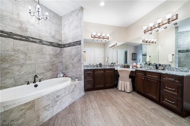 bathroom with vanity, a chandelier, and tiled bath