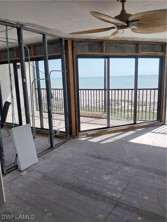 unfurnished sunroom featuring ceiling fan and a water view