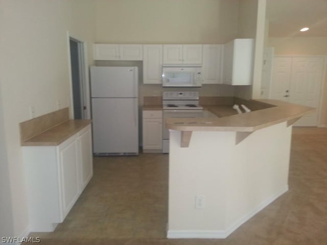 kitchen with white appliances, kitchen peninsula, white cabinetry, and a breakfast bar area