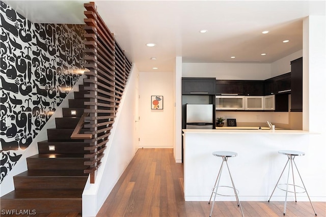 kitchen featuring a kitchen breakfast bar, hardwood / wood-style floors, kitchen peninsula, and stainless steel refrigerator