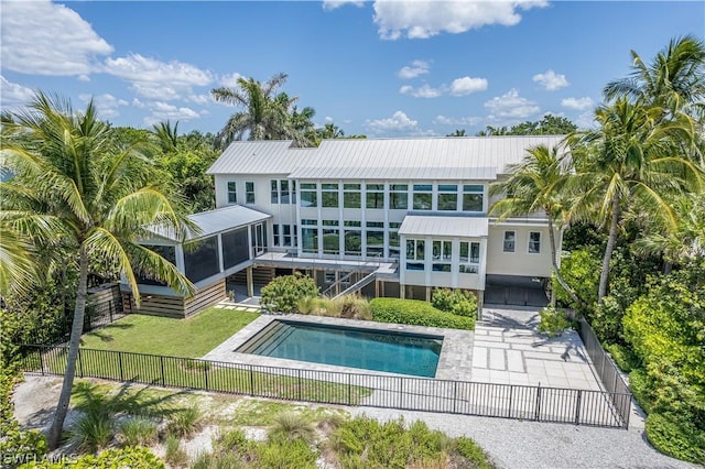 back of property with a sunroom, a fenced in pool, and a lawn