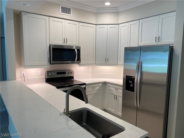 kitchen featuring ornamental molding, appliances with stainless steel finishes, white cabinetry, light stone counters, and sink