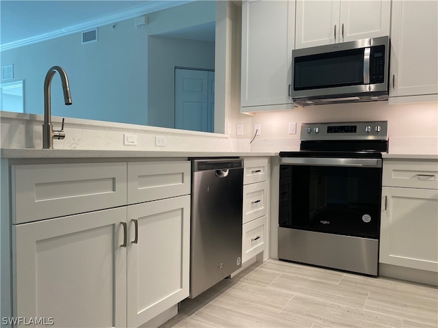 kitchen featuring white cabinetry, light hardwood / wood-style floors, appliances with stainless steel finishes, and crown molding