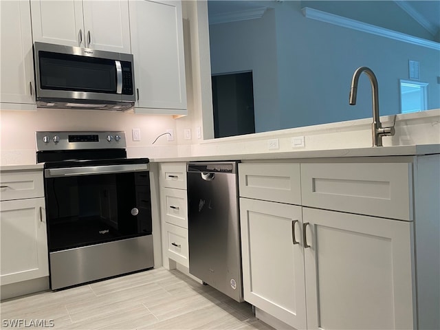 kitchen with stainless steel appliances, white cabinets, and ornamental molding