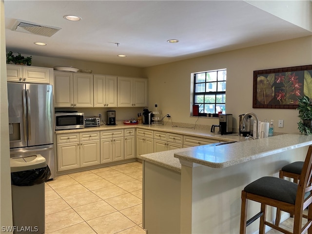 kitchen with light tile flooring, kitchen peninsula, a breakfast bar, white cabinetry, and appliances with stainless steel finishes