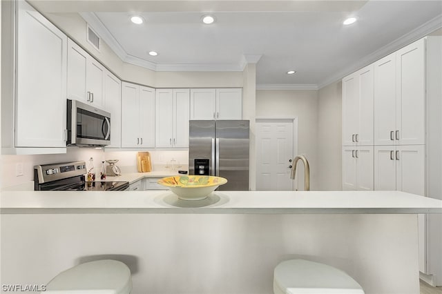 kitchen with white cabinets, a kitchen bar, ornamental molding, and stainless steel appliances