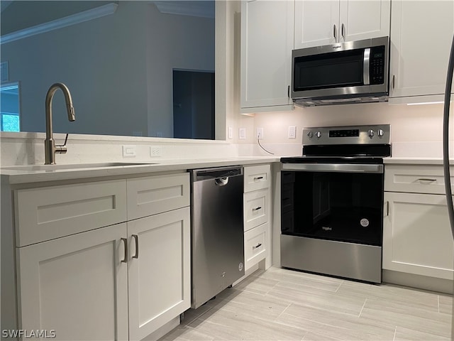 kitchen with ornamental molding, stainless steel appliances, white cabinetry, and sink