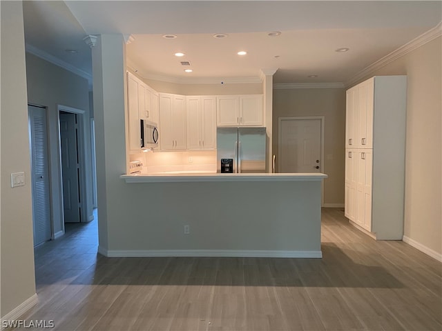 kitchen with crown molding, white cabinets, appliances with stainless steel finishes, and hardwood / wood-style flooring