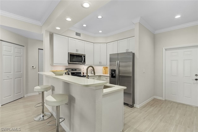 kitchen with a breakfast bar area, kitchen peninsula, appliances with stainless steel finishes, and white cabinetry