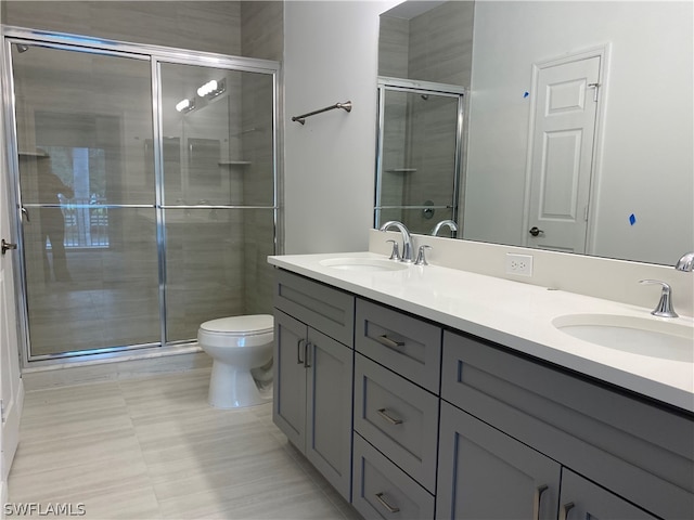 bathroom with toilet, tile flooring, dual vanity, and a shower with shower door