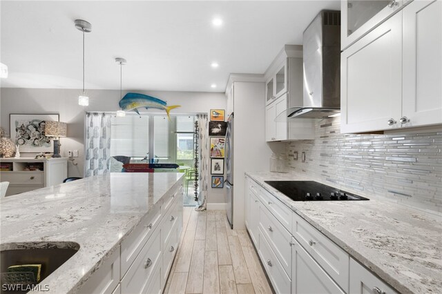 kitchen featuring white cabinetry, wall chimney exhaust hood, light hardwood / wood-style flooring, decorative light fixtures, and black electric stovetop