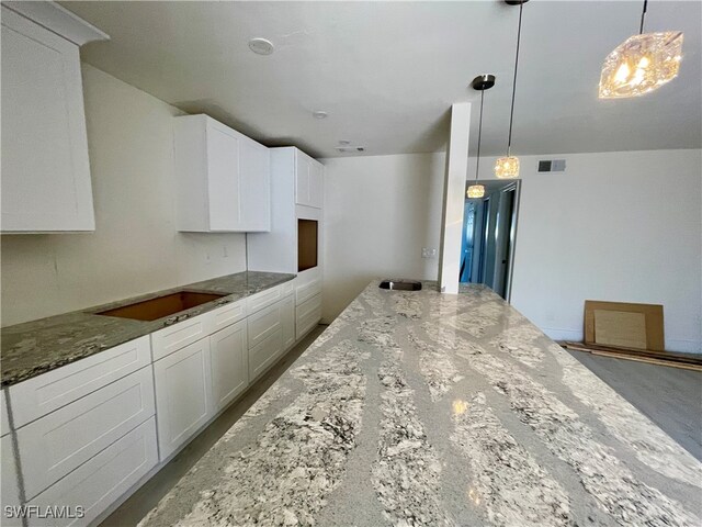 kitchen featuring stone countertops, white cabinetry, decorative light fixtures, and black stovetop