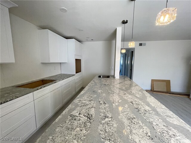 kitchen with hardwood / wood-style floors, decorative light fixtures, black electric cooktop, stone countertops, and white cabinetry