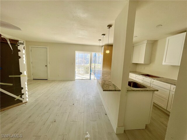 kitchen featuring white cabinetry, sink, hanging light fixtures, stovetop, and light hardwood / wood-style floors