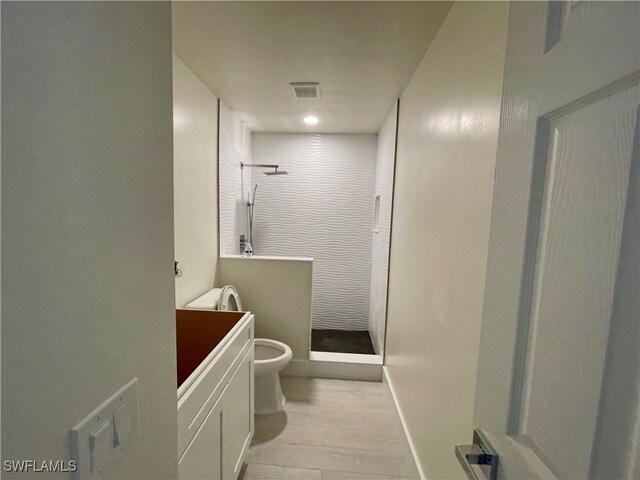 bathroom featuring toilet, hardwood / wood-style floors, vanity, and tiled shower