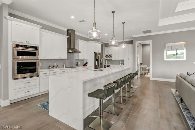 kitchen featuring decorative light fixtures, backsplash, appliances with stainless steel finishes, a breakfast bar, and wall chimney range hood