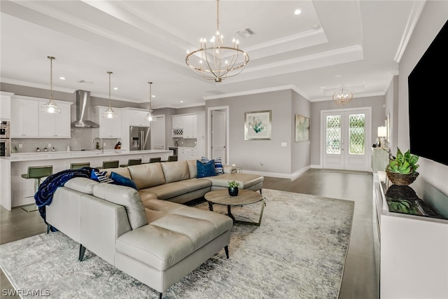 living room featuring a chandelier, a raised ceiling, ornamental molding, and french doors