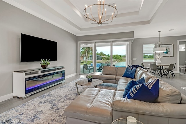 living room featuring a raised ceiling, an inviting chandelier, and ornamental molding