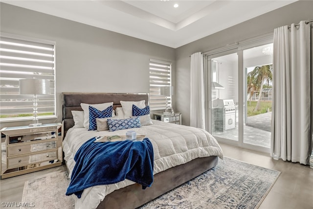 bedroom featuring a raised ceiling, access to outside, and light wood-type flooring