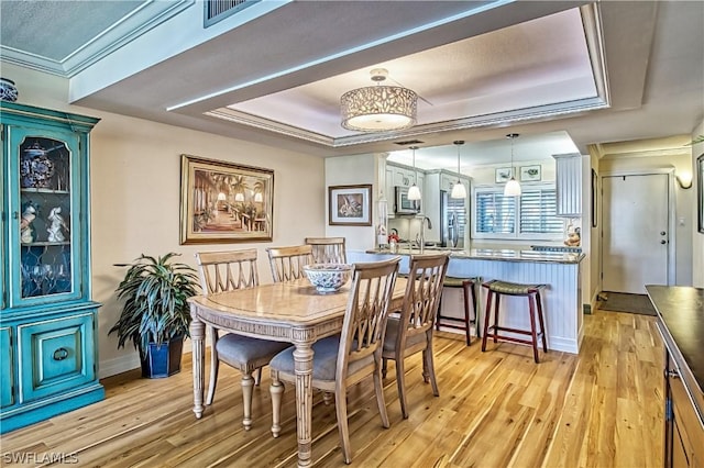 dining space with crown molding, a tray ceiling, and light hardwood / wood-style flooring