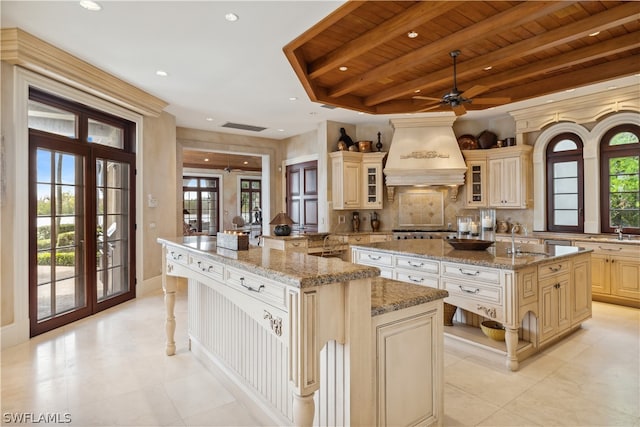 kitchen with cream cabinets, custom exhaust hood, and a center island with sink