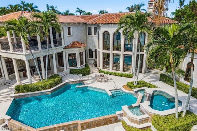 rear view of property with a patio, a balcony, an in ground hot tub, and an outdoor fire pit