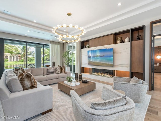 living room featuring a lit fireplace, a tray ceiling, light wood-style floors, a notable chandelier, and recessed lighting