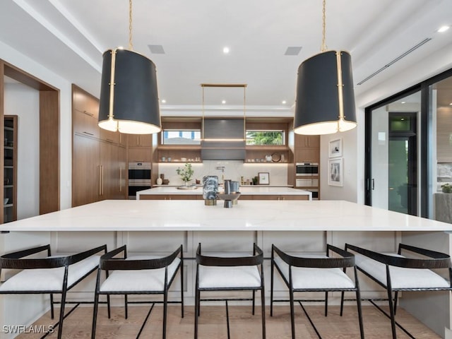 kitchen with exhaust hood, hanging light fixtures, a large island, tasteful backsplash, and brown cabinetry