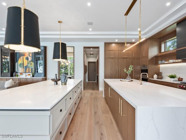 kitchen featuring light stone counters, a spacious island, light wood-style floors, brown cabinetry, and modern cabinets
