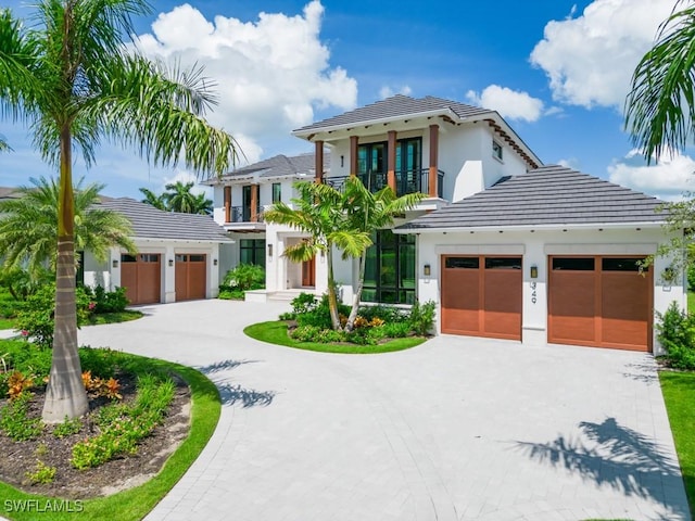 view of front of home featuring a balcony, a garage, a tiled roof, decorative driveway, and stucco siding