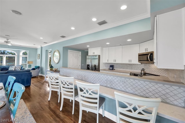 kitchen with dark hardwood / wood-style floors, ceiling fan, crown molding, white cabinets, and stainless steel appliances