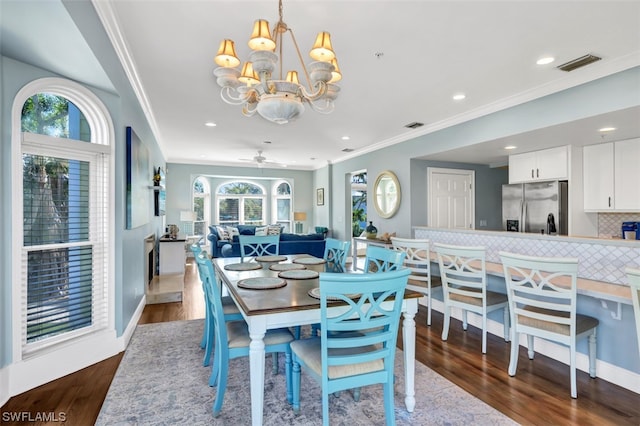 dining room with ceiling fan with notable chandelier, crown molding, and dark wood-type flooring